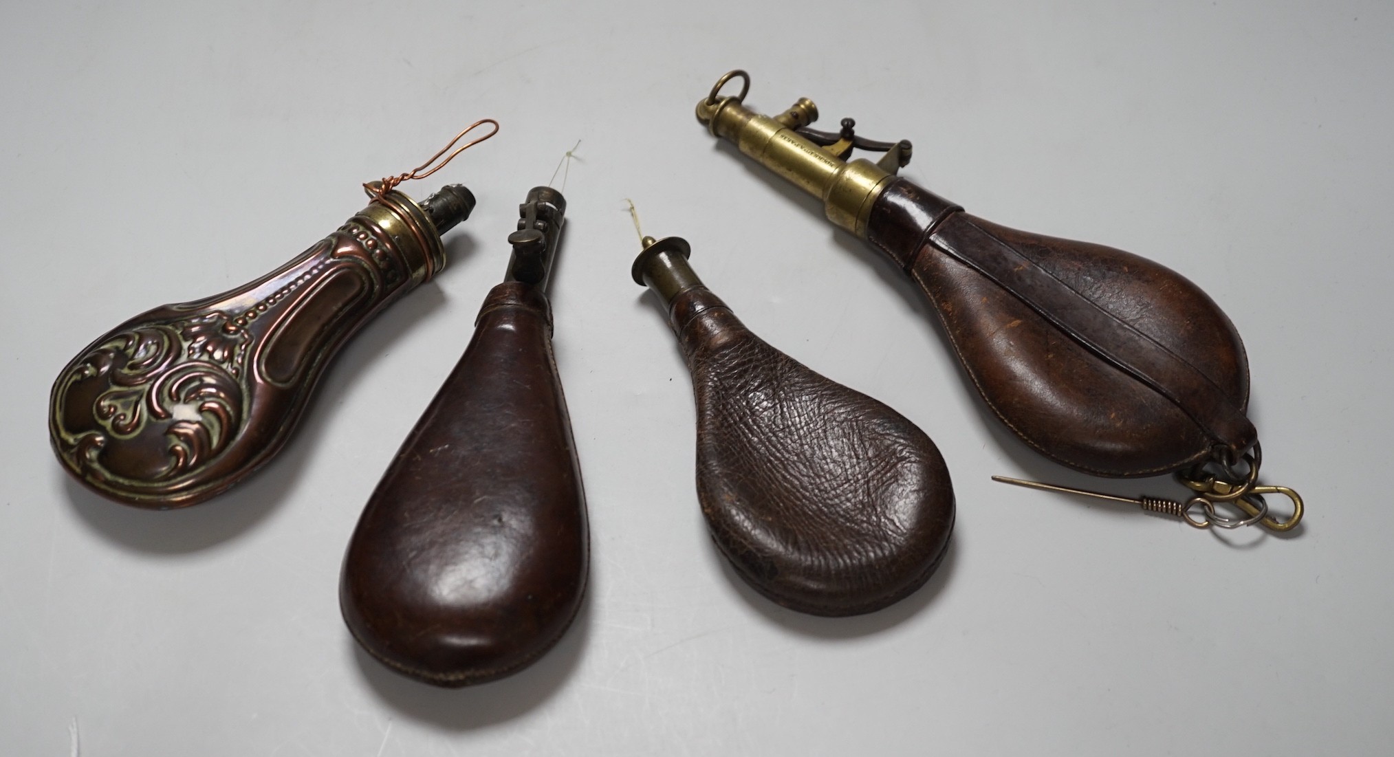 Four brass mounted powder flasks, to include three leather flasks, and one copper. Largest 24cm long